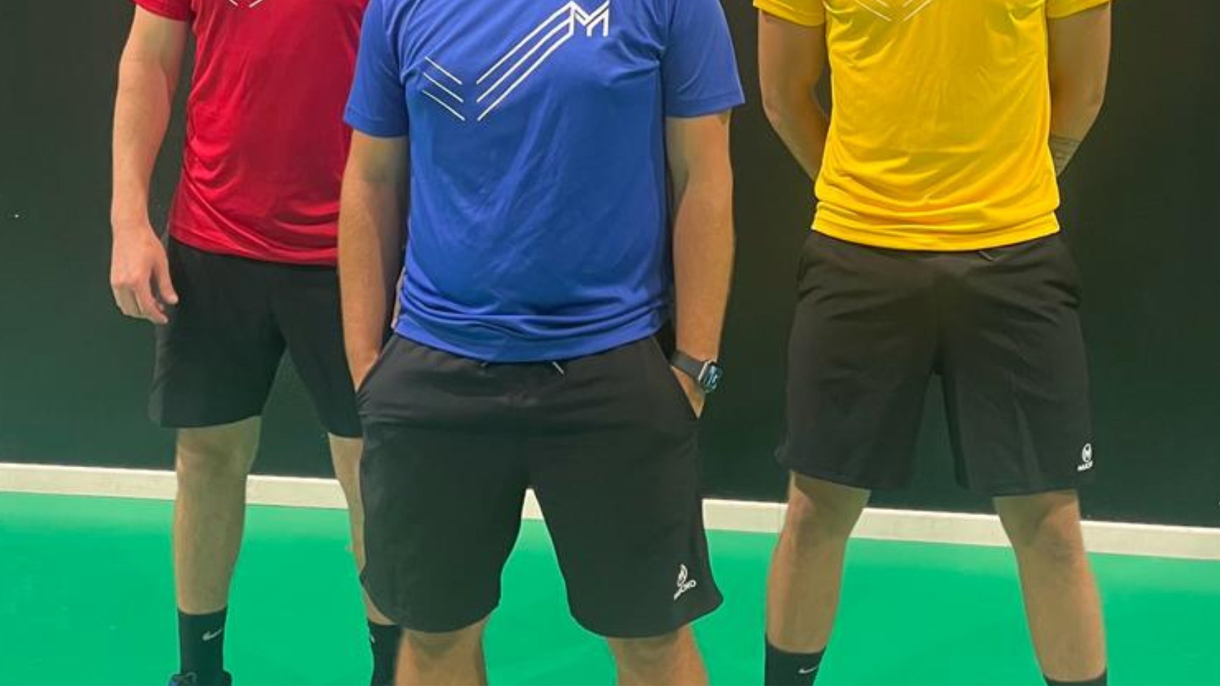 Jeune homme vêtu d'un short blanc et d'une chemise de sport jaune, tous deux de la marque Mucho, faisant de l'exercice avec un ballon de poids dans une salle d'exercice avec un plancher en bois et des miroirs en arrière-plan