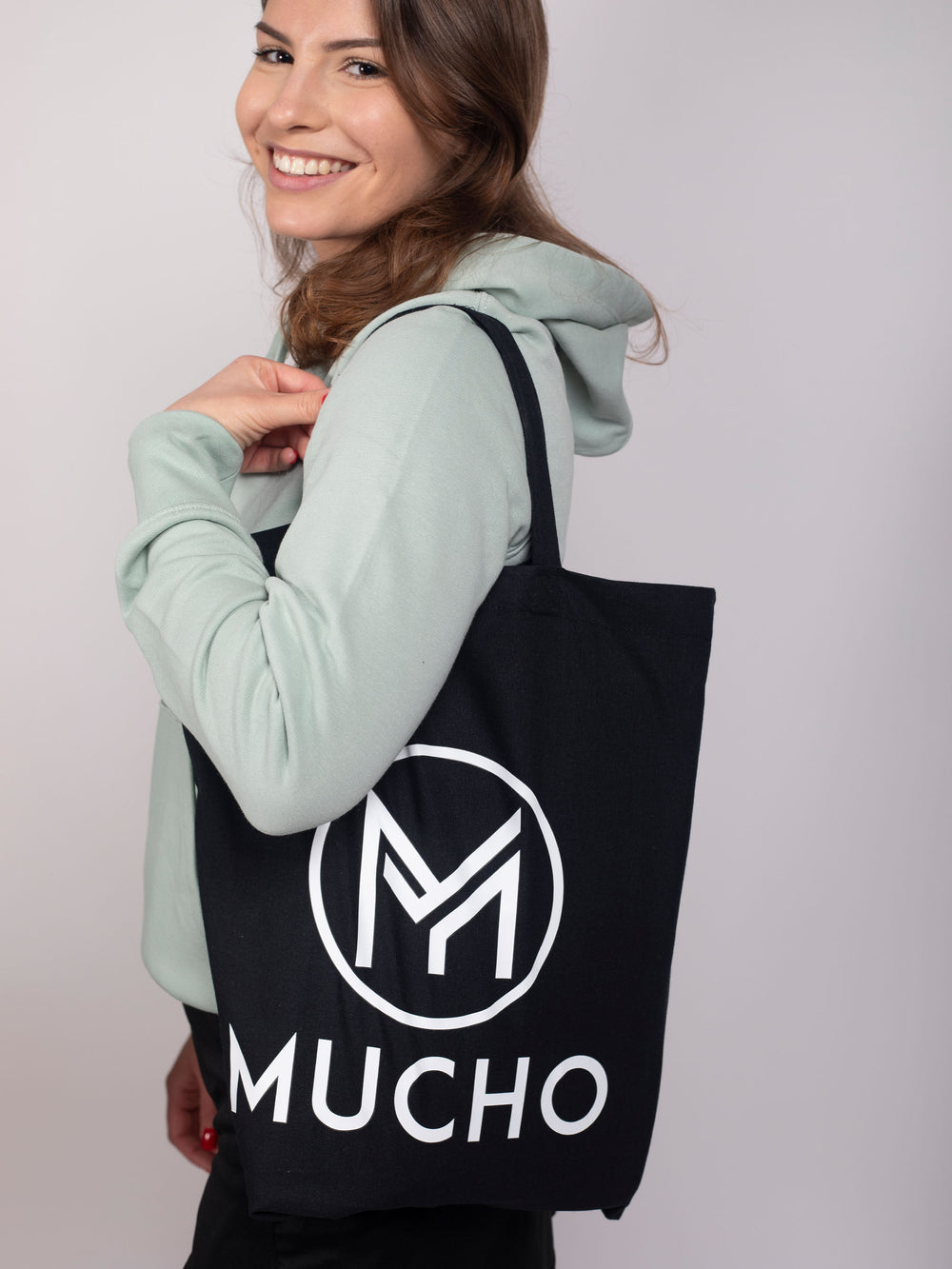 Femme souriante vêtue d'un sweat à capuche et portant un sac Cabas en coton de la marque Mucho.Shop